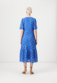 Lace dress in bright blue, featuring short sleeves, a tiered skirt, and floral patterns. Complements with nude strappy heels.