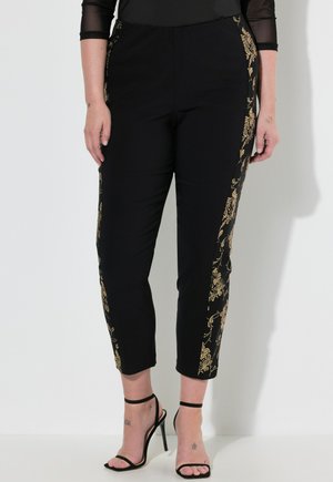 Pantaloni neri con ricamo floreale dorato sui lati, caratterizzati da una vestibilità rilassata e una lunghezza cropped. Texture liscia con una cintura elastica.