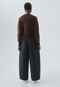 Pull cropped marron avec des poignets et un ourlet côtelés, accompagné d'un pantalon large gris foncé. Tissu lisse et coupe décontractée.