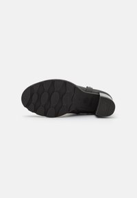 Suela de zapato negra con goma texturizada, que presenta patrones ovalados y un leve tacón. Marcada con "ANTI SLIDE" para mejorar la adherencia.