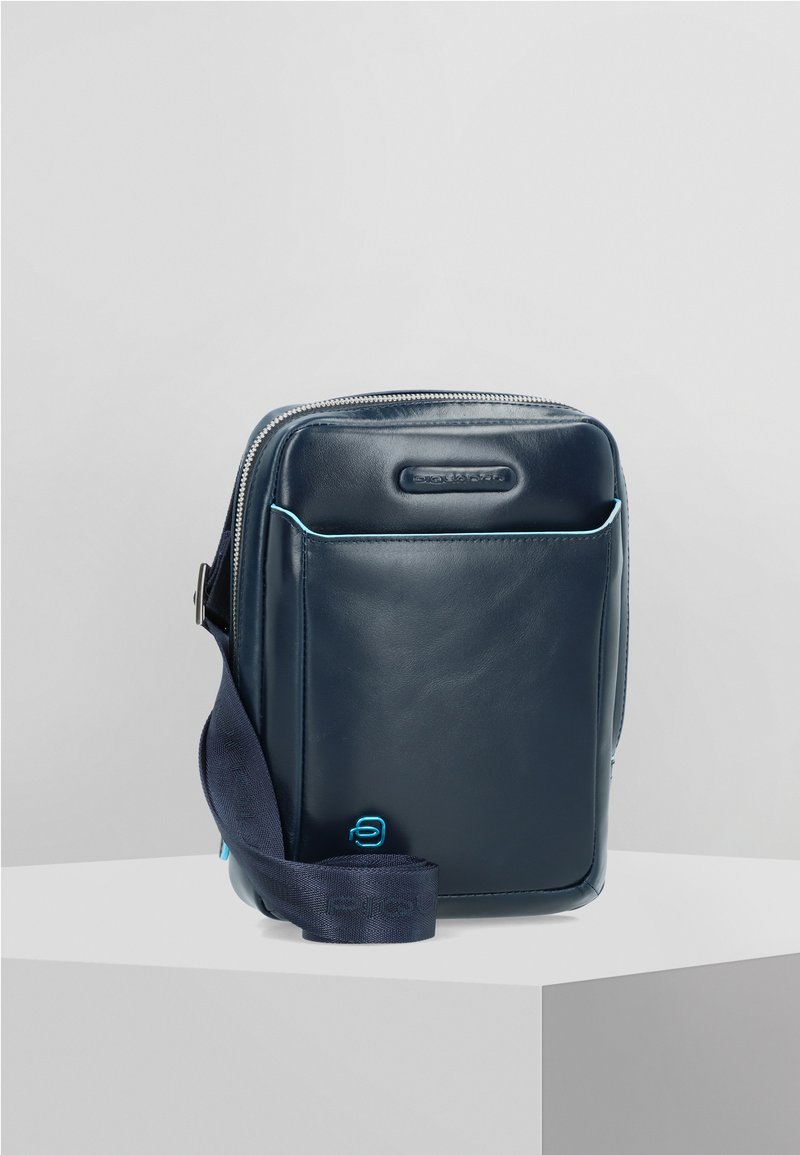 Marineblaue Leder-Crossbody-Tasche mit Reißverschluss, Fronttasche, hellblauen Akzentstreifen und Stoffgurt. Glatte Textur mit minimalistischem Design.