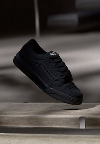 Schwarze Sneaker mit einem glatten synthetischen Obermaterial, das mit durchlöcherten Akzenten, flachen Schnürsenkeln und einer strukturierten Gummisohle versehen ist.