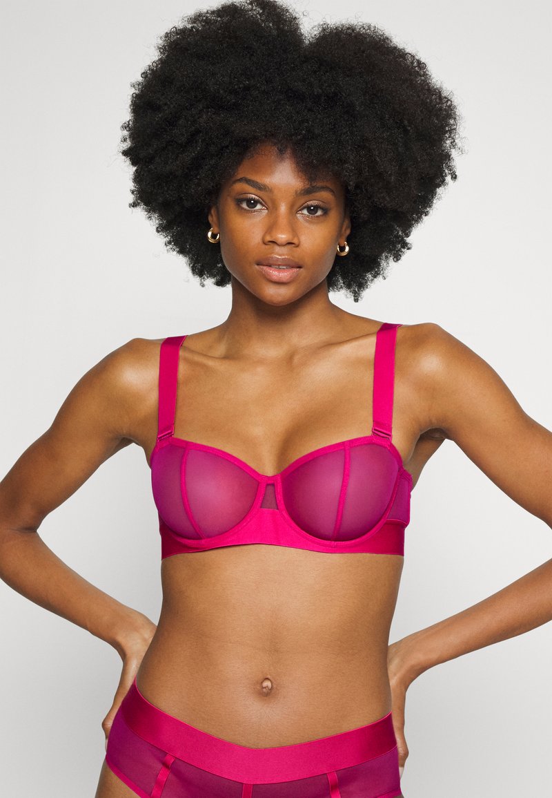 Sutiã fúcsia com aro, painéis de rede transparentes, copas almofadadas, alças ajustáveis e uma costura horizontal ao centro. Cueca de cintura alta combinando.