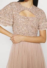 Vestido de noche con cuentas en rosa suave, que presenta lentejuelas, mangas cortas con vuelo, un escote en forma de lágrima y una falda plisada.
