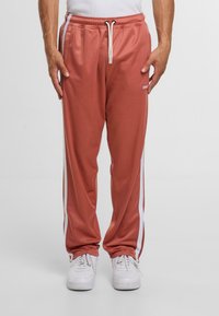 Rosa Jogginghosen mit weißen Seitenstreifen, elastischem Bund und Kordelzug. Hergestellt aus glattem, leichtem Stoff.