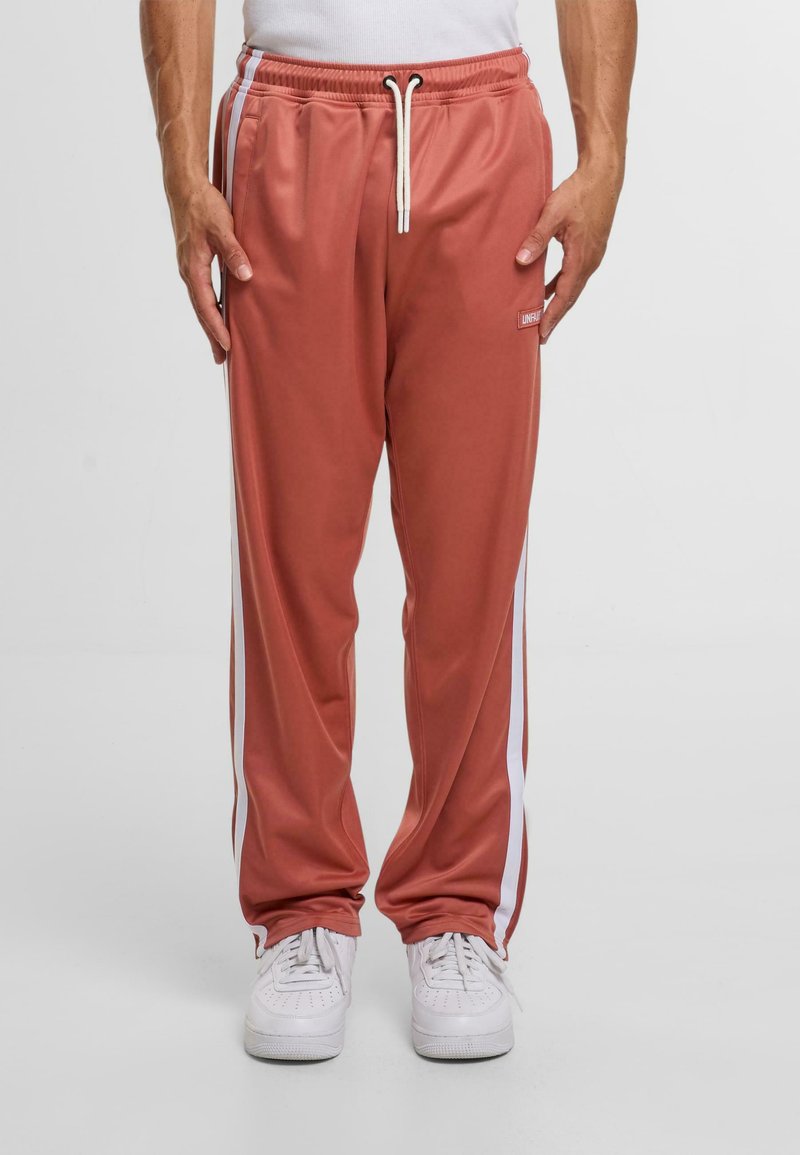 Rosa Jogginghosen mit weißen Seitenstreifen, elastischem Bund und Kordelzug. Hergestellt aus glattem, leichtem Stoff.