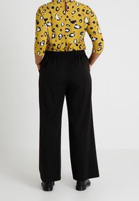 Pantalon noir à jambes larges avec une taille élastique, associé à un haut jaune imprimé léopard avec des manches trois-quarts et un dos ajouré.