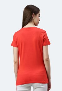 T-shirt rossa in cotone con maniche corte e scollatura a girocollo, caratterizzata da una texture liscia e un orlo posteriore leggermente più lungo.