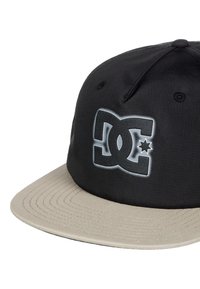 Schwarze Kappe mit einem beigen Schirm. Hat ein auffälliges graues DC-Logo auf der Vorderseite. Hergestellt aus glattem Stoff mit einer strukturierten Form und genähten Details.