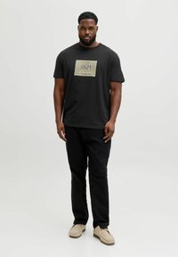 Sort bomuld t-shirt med et gyldent rektangulært logo, parret med sorte bukser og beige sko. Enkel, rund hals-stil.