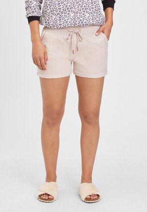 Helles rosa Baumwollshorts mit einem Kordelzugbund und umgeschlagenen Säumen, kombiniert mit beigen, mit Fell gefütterten Slides. Taschen auf jeder Seite.