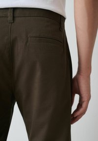 Tumši brūni piegriezti bikses ar gludu tekstūru, ar aizmugures kabatu, šauru piegriezumu un redzamu jostu cilpu tuvumā jostasvietai.