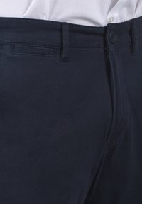 Pantalons bleu marine en mélange de coton, dotés d'une fermeture à bouton, de passants de ceinture et d'une texture lisse avec un éclat subtil.