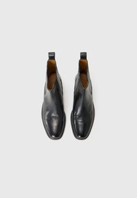 Svarte skinn ankelstøvler med en glatt overflate, med elastiske sidestykker og en rund tå. Flat såle og minimal sømdetalj.