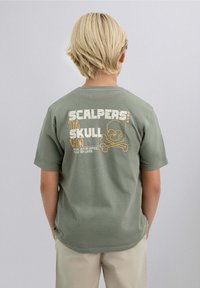 Camiseta de algodón verde oliva con mangas cortas. La parte posterior presenta un gráfico de calavera y tibias cruzadas con el texto "SCALPERS! The SKULL crew" en amarillo y blanco.