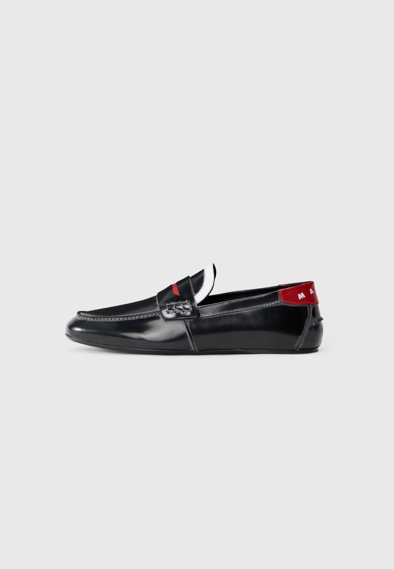 Sapatos loafers de couro preto com acabamento suave, apresentando um detalhe vermelho na parte de trás e costura decorativa na frente. Sola plana.
