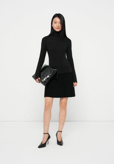 Fekete garbós pulóver, bordázott fekete szoknya, fekete clutch táska és fekete magassarkú cipő, egy modellen egy fehér háttér előtt.