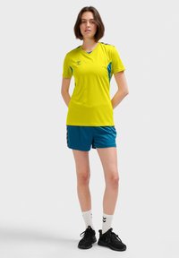 Gul tränings-T-shirt med blåa detaljer, tillsammans med turkosa shorts. Båda plaggen har en sportig design och ett lätt tyg.