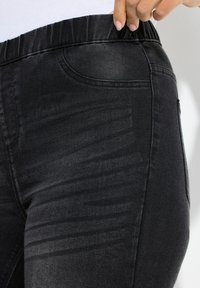 Czarne jeansy z elastycznym pasem, o gładkiej fakturze i delikatnym przetarciu wzdłuż nogawki. Widoczne dwie boczne kieszenie.