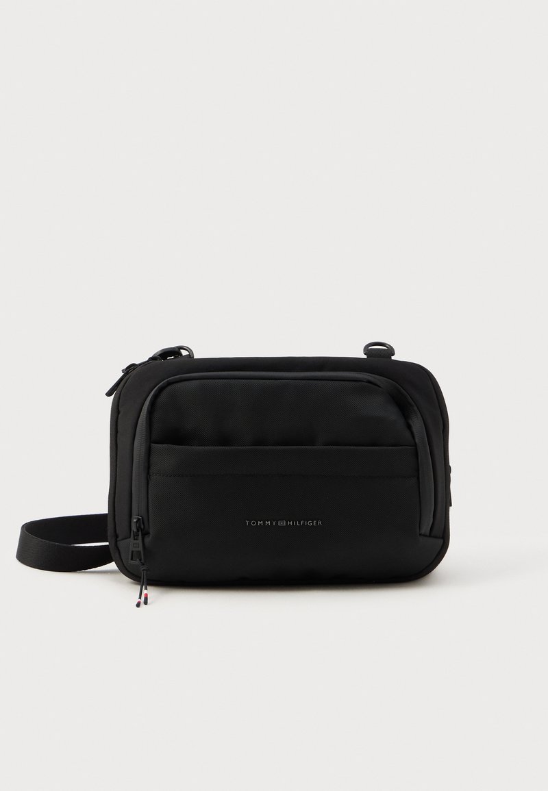 Čierna crossbody taška s textúrovanou tkaninou, hlavnou zipsovou priehradkou, prednou vreckom a nastaviteľným popruhom. Obsahuje logo Tommy Hilfiger.