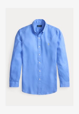 Gai zilo garo piedurkņu pogājamo krekls, kas izgatavots no lins. Tam ir klasiskā apkakle, baltas pogas un neliels dzeltenas krāsas logo uz krūtīm.