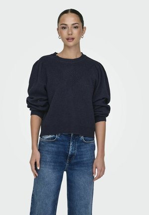 Pull en tricot bleu marine foncé avec des manches bouffantes, un col côtelé et des points de couture texturés. Assorti avec un jean droit bleu clair.
