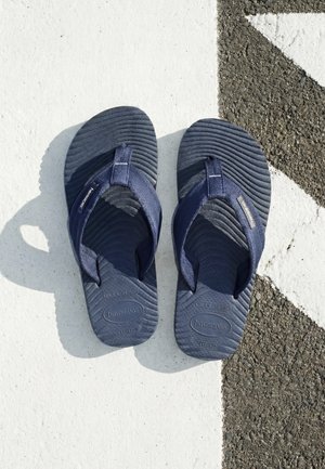 Coppia di infradito Havaianas blu scuro su un pavimento bianco e nero testurizzato con linea diagonale.