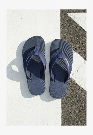 Coppia di infradito Havaianas blu scuro su un pavimento bianco e nero testurizzato con linea diagonale.