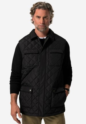 Schwarze gesteppte Weste mit Kragen, Frontreißverschluss, zwei Brusttaschen und zwei unteren Taschen. Getragen über einem schwarzen Pullover.