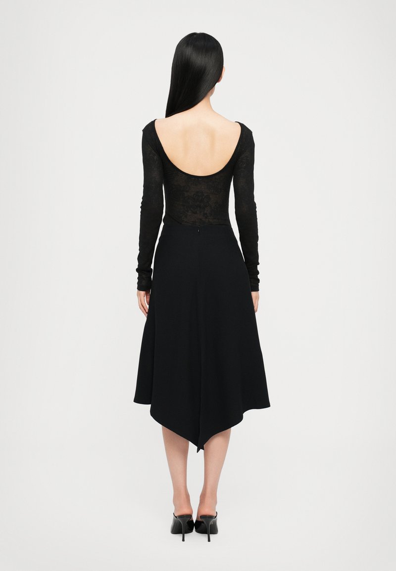 Abito nero con un body trasparente a maniche lunghe e scollatura profonda sulla schiena, abbinato a una gonna fluida e asimmetrica.