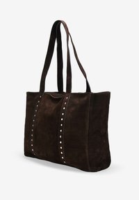 Bolso tote de ante marrón con dos correas largas, presenta tachuelas plateadas a lo largo de las costuras frontales, forma rectangular y textura suave.