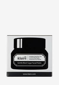 Svart burk med en vit etikett. Texten inkluderar "Mild svart socker ansiktsskrubb", som beskriver exfolierande och fuktgivande egenskaper.