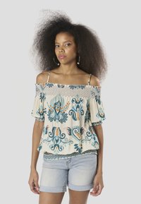 Blusa de hombros descubiertos en color crema con bordado floral en verde azulado y naranja, con detalles fruncidos y mangas cortas. Combinada con pantalones cortos de mezclilla.