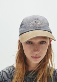 Căciulă gri închis cu visieră bej, având brodat textul "SimStudio STREETWEARDEPT" în roz deschis, realizată din material de bumbac.