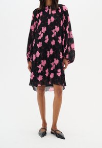 Svart plisserad klänning med rosa blommönster, långa puffärmar och en nyckelhålsringning. Buren med svarta spetsiga ballerinas.