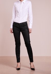 Svarta tajta byxor med en slät yta, med framfickor, knapprar och en avsmalnande design, i kombination med en krispig vit skjorta.