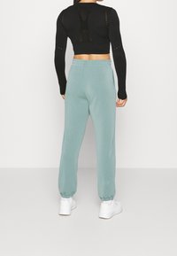Top nero corto a maniche lunghe con schiena in rete e ritagli, abbinato a pantaloni sudati verde chiaro a gamba stretta con polsini elastici. Sneakers bianche.
