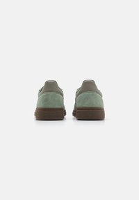 Chaussures en daim vert avec des semelles en caoutchouc marron et un talon en cuir lisse. Le design présente une forme arrondie et des embellissements minimaux.