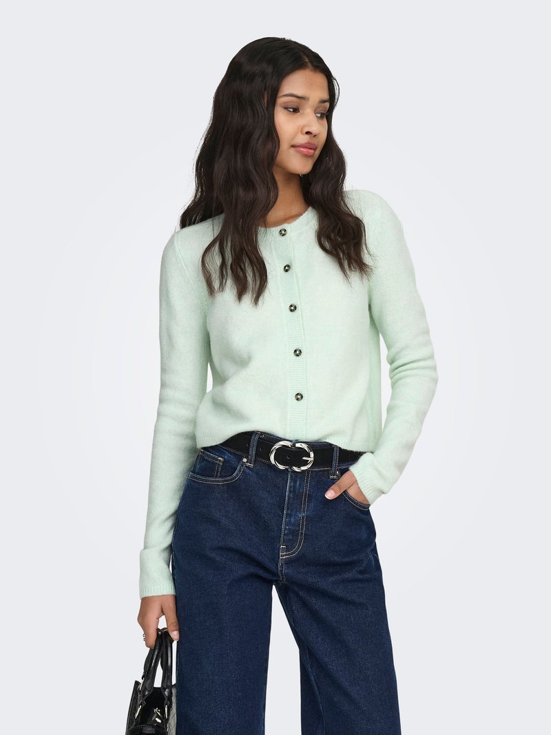 Minzgrüner Cardigan mit schwarzen Knöpfen, kombiniert mit hoch taillierter, dunkler Denim-Jeans und einem schwarzen Gürtel. Strukturierter Stoff und tailliertes Design.