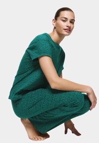 Zestaw dresowy w zielone kropki wykonany z miękkiego materiału; bluzka z krótkim rękawem i okrągłym dekoltem oraz luźne spodnie z elastycznym pasem.