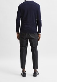 Marinblå stickad tröja, långa ärmar, rundad hals, tillsammans med mörkgrå tapered-byxor, synliga sömdetaljer, och svarta skor.