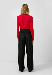 Rode top met lange mouwen, gecombineerd met hoge taille, wijde zwarte broek met een subtiele glans. De outfit heeft een gestroomlijnde silhoett.