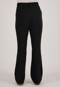 Achteraanzicht van een persoon die zwarte broek met hoge taille, achterzakken en uitlopende pijpen draagt, staand op een neutrale achtergrond.