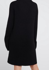 Czarna dzianinowa sukienka z prążkowanym wzorem, długimi rękawami i luźnym krojem, kończąca się powyżej kolan.