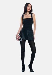 Zwarte mouwloze top met vierkante halslijn, geplooide details; zwarte leren minirok; ondoorzichtige zwarte panty; stiletto hakken; zilveren handtasje.