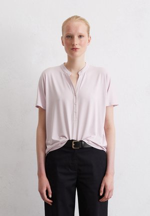 Lichtroze T-shirt met korte mouwen en een knoopjes henley halslijn. Gecombineerd met zwarte broek en een zwarte riem met een gouden gesp. Glad textuur.