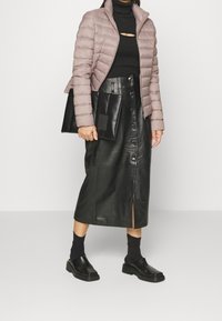 Veste matelassée violet clair, col roulé noir, jupe midi en cuir noir avec des boutons à l'avant, et chaussures noires chunky avec une semelle texturée.