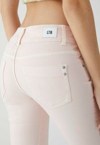Světlé růžové džínové kalhoty s hladkou texturou, s kapsami na zadní straně zdobenými bílým prošíváním a stříbrnými knoflíky. Štítek nese nápis "LTB".