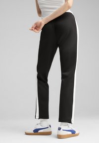 Czarne dresy z białymi paskami po bokach, elastyczny pas, zwężane nogawki, gładka faktura, krótsza długość, w zestawie z białymi trampkami.