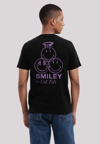 Schwarzes Baumwoll-T-Shirt mit drei lila Smiley-Gesichtern auf der Rückseite, darunter der Text "SMILEY" und "circa Ltd.Ed".